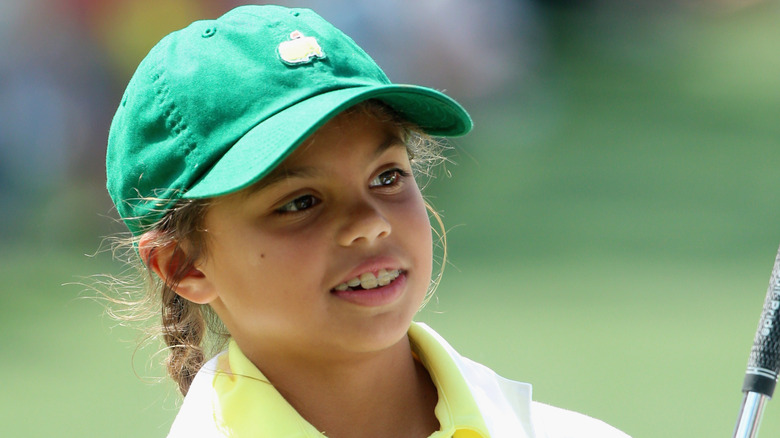 Sam Woods as a young child wears a green baseball hat on a golf course