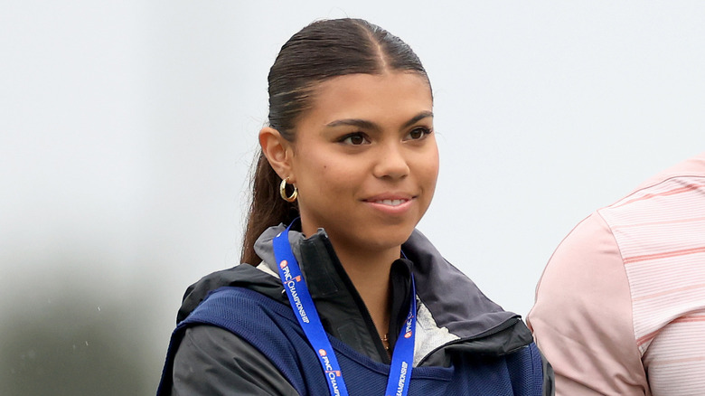 Sam Woods stands next to her dad smiling outside looking into the distance at a golf tournament