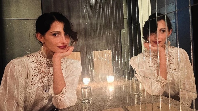 Audrey McGraw posing in front of a mirror with her hand on her chin wearing white