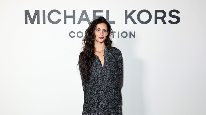 Audrey McGraw posing on the red carpet at a Michael Kors fashion show wearing a black and gray dress