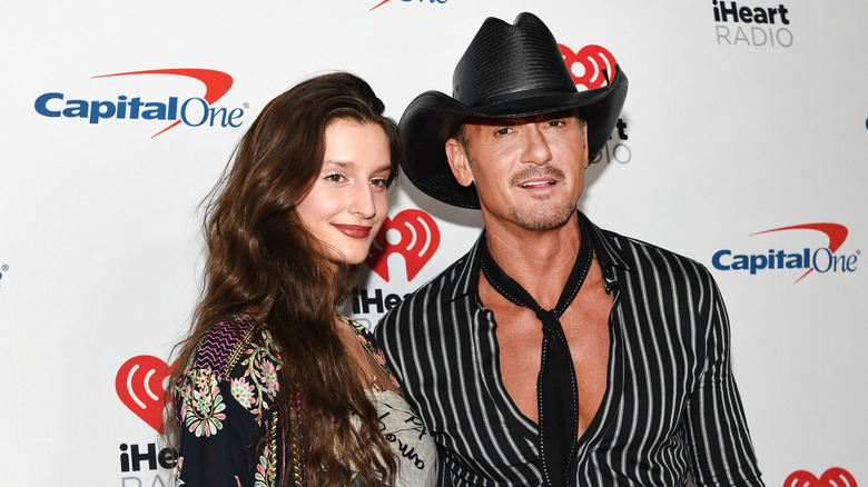 Tim McGraw's daughter Audrey standing next to him on the red carpet with her hair down while he wears a cowboy hat and tie