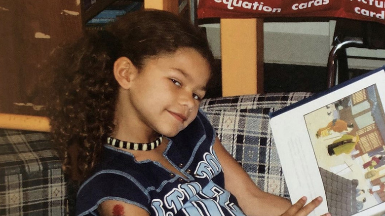 Zendaya as a kid smirking with an open picture book in her lap.