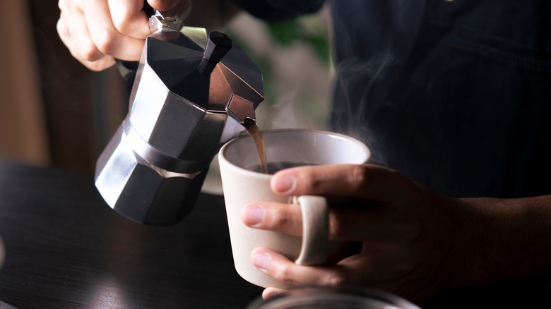 Person pours coffee from a pot into a mug