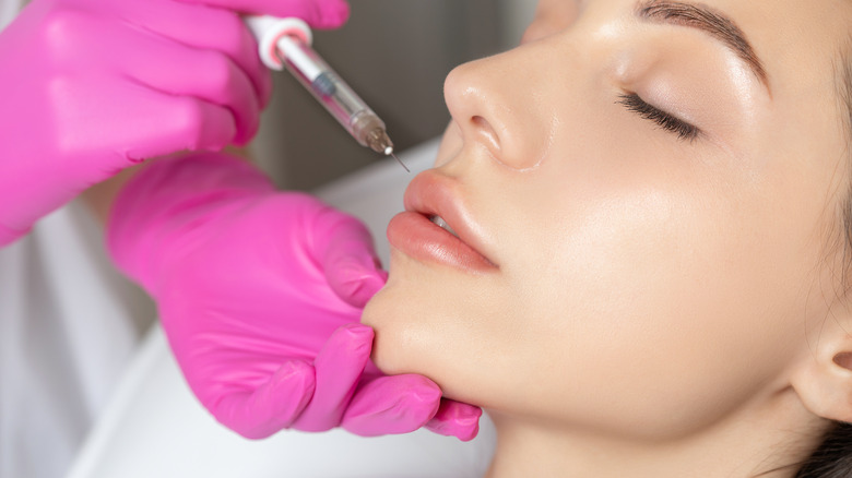 A gloved hand injecting filler into a woman's lips