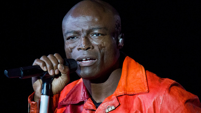Seal sings into a microphone while wearing an orange jacket.