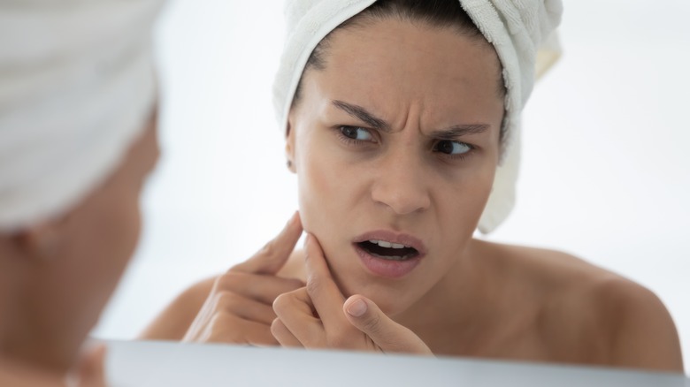 woman looking at her breakouts in the mirror