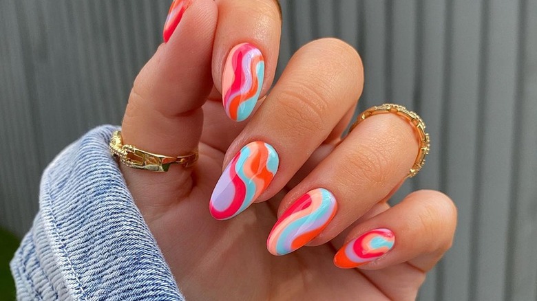 Hand showing nails with multicolor swirl manicure in peach, magenta, lavender, orange and blue
