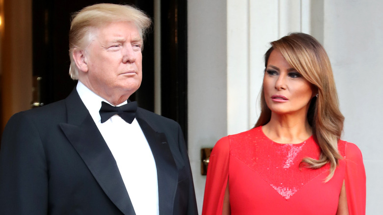 Donald Trump wearing a tuxedo and Melania Trump wearing a red dress with cape sleeves.