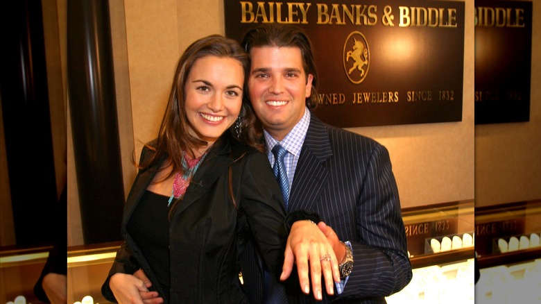 Donald Trump Jr. holding Vanessa Trump's hand out to show off her engagement ring in front of a Bailey Banks & Biddle sign.