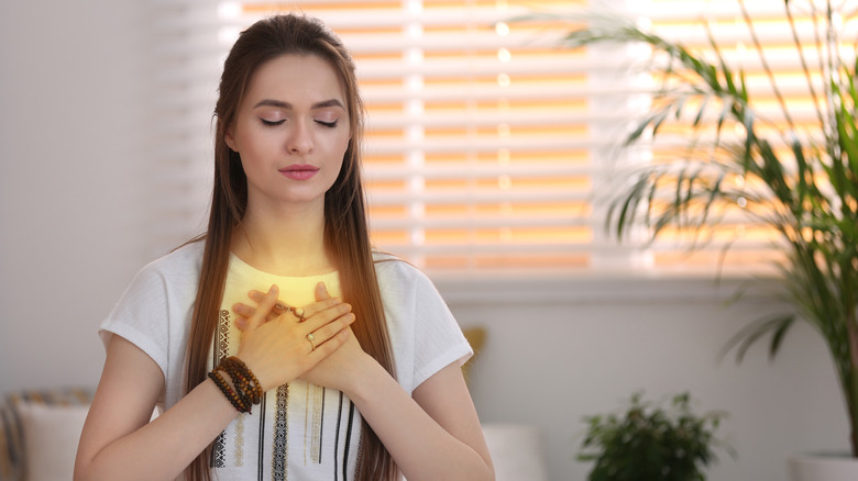 Woman sitting with her eyes closed and hands over her heart