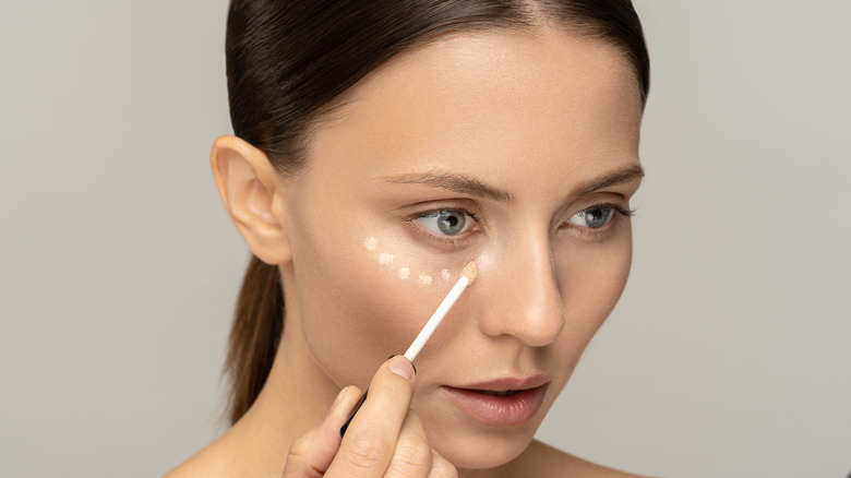 Brunette woman with her hair pulled back applying concealer.