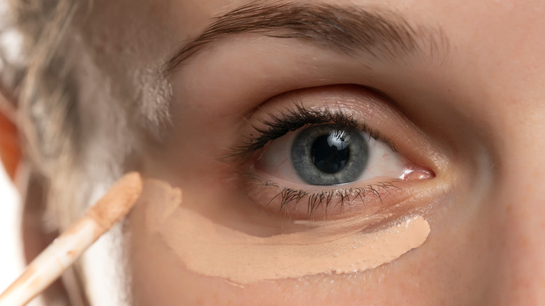 Closeup picture of a young woman applying concealer around her eye