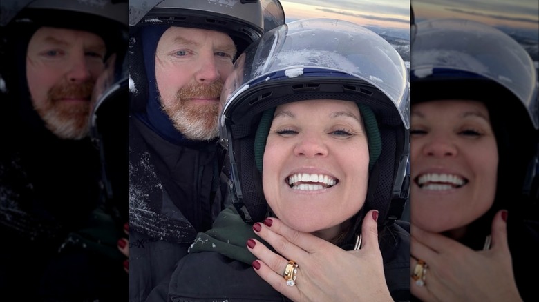 Don Reidy and Leslie Davis wearing motorcycle helmets while Davis smiles and shows off her ring