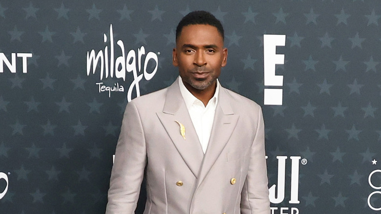 Justin Sylvester in a gray suit posing on the E! red carpet