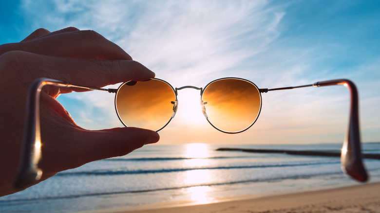 Sunglasses being held up over the sunlight ocean 