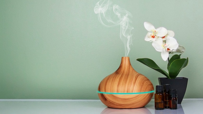 A wooden essential oil diffuser with mist next to an orchid