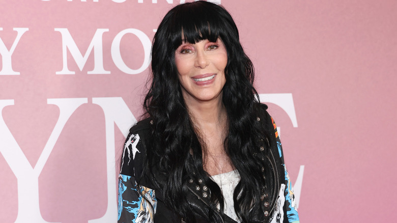 Cher smiling for photographs in a multicolored leather jacket