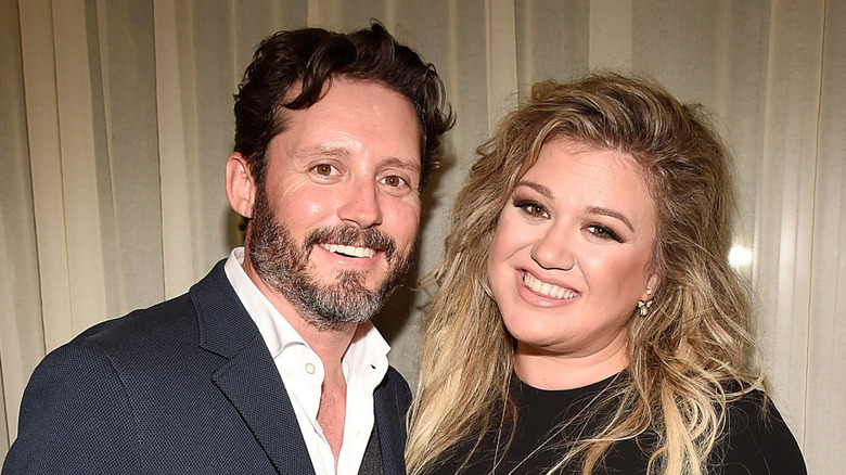 Brandon Blackstock smiling in a suit next to Kelly Clarkson who's in a black dress.