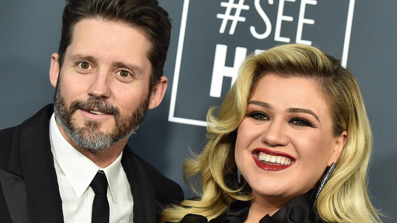 Brandon Blackstock smiling in a suit next to Kelly Clarkson in a black dress.