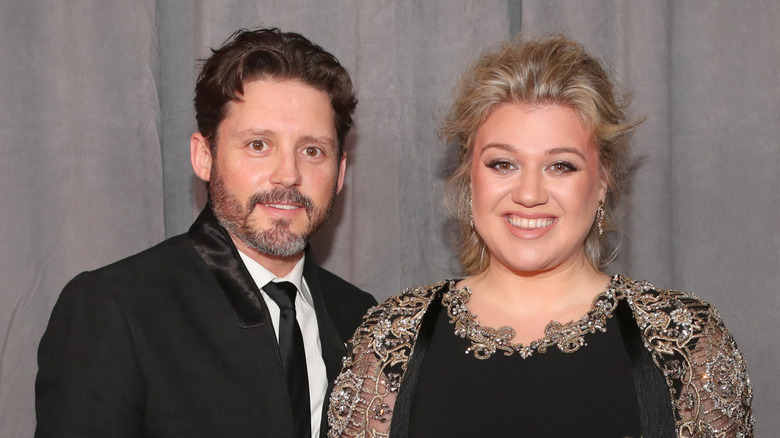 Kelly Clarkson in a black and gold dress posing next to Brandon Blackstock who's in a suit