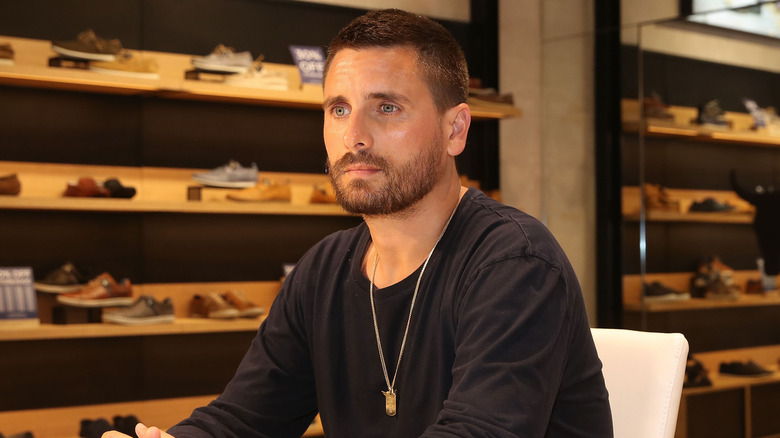 Scott Disick sitting amid wooden shelves full of shoes in November 2018