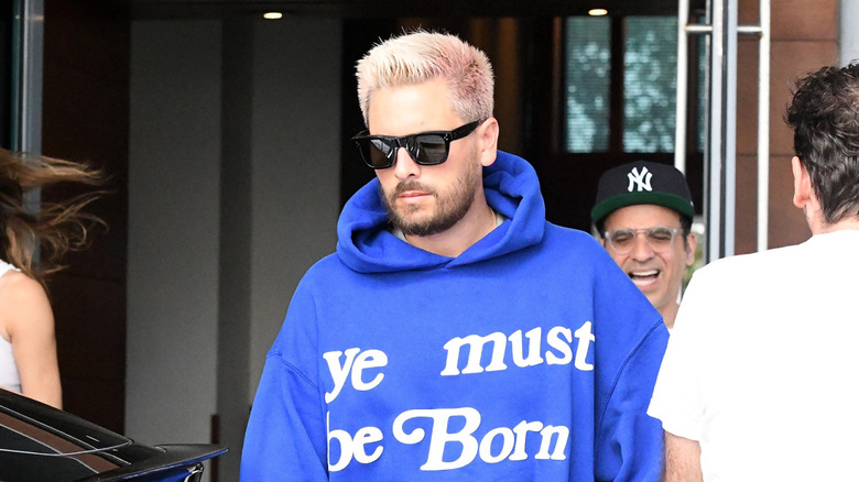 Scott Disick walking outside with dyed blond and pink hair and sunglasses in March 2021