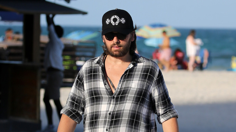 Scott Disick walking on the beach in a ballcap and dark sunglasses in July 2022