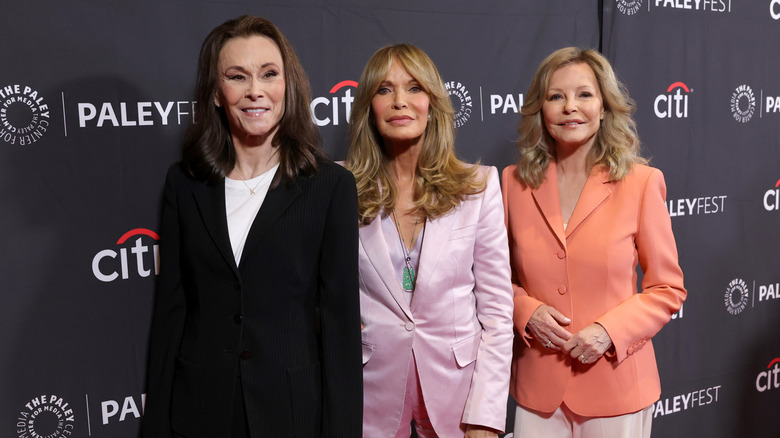 Kate Jackson, Jaclyn Smith and Cheryl Ladd posing in black, pink, and coral blazers, respectively.