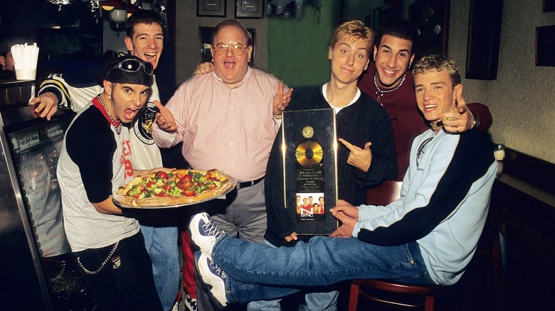 Chris Kirkpatrick holding a pizza with JC Chasez, Lou Pearlman, Lance Bass holding a gold record, Joey Fatone, and Justin Timberlake