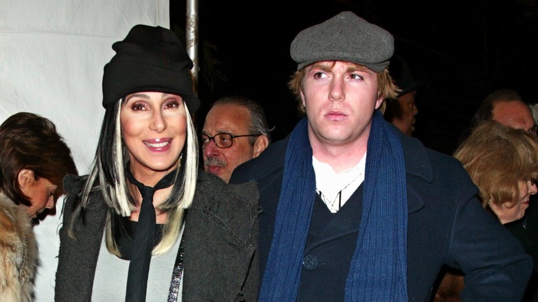 Elijah Blue Allman in newsboy cap and blue scarf with Cher in black knit cap and necktie