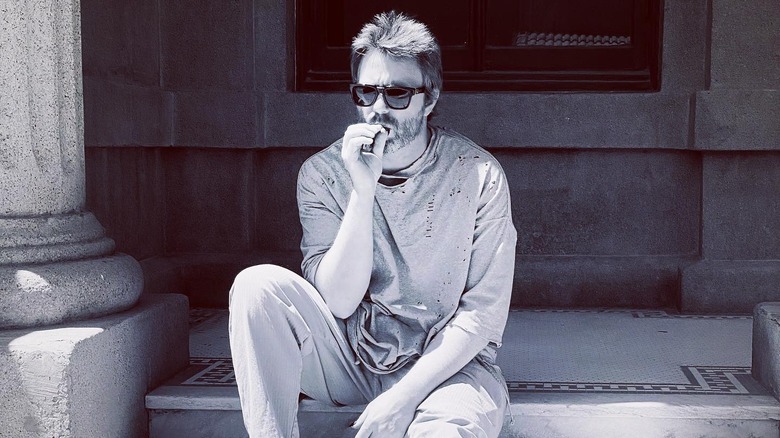 Elijah Blue Allman sitting on steps wearing sunglasses and smoking
