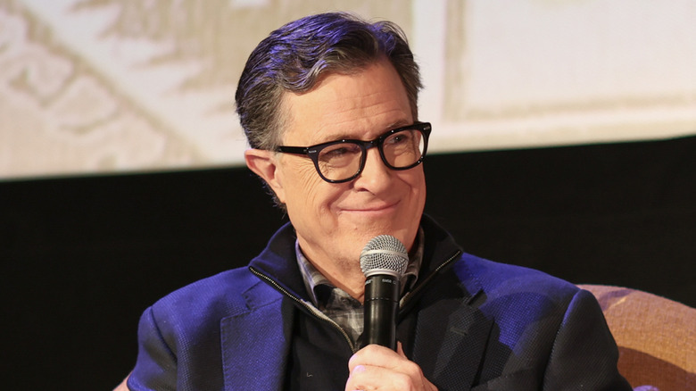 Closeup of Stephen Colbert holding microphone and grinning mischievously