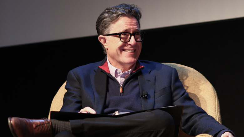 Stephen Colbert laughing on stage in an arm chair
