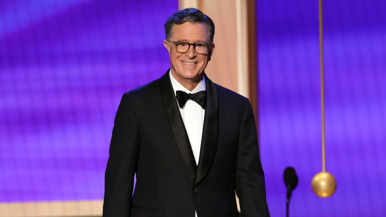 Stephen Colbert smiling on stage in tuxedo