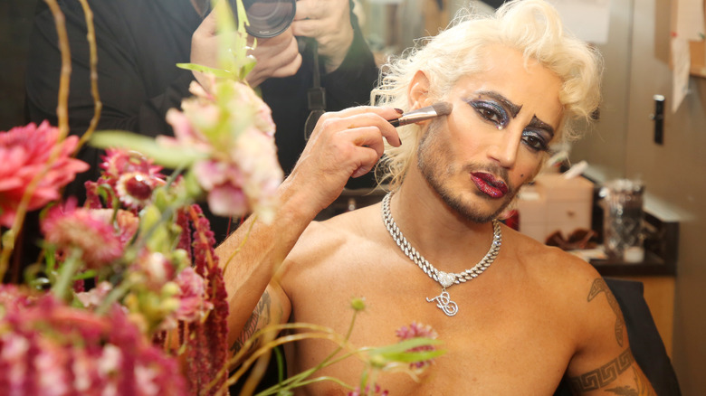 Frankie Grande putting on makeup in a mirror, shirtless.