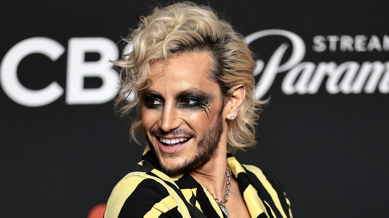 Frankie Grande in black eye makeup and a yellow and black jacket, looking over his shoulder.