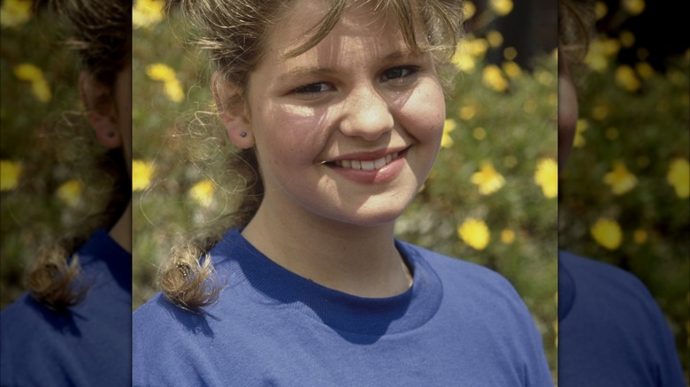 Candace Cameron Bure in the '80s with bangs forcing a smile