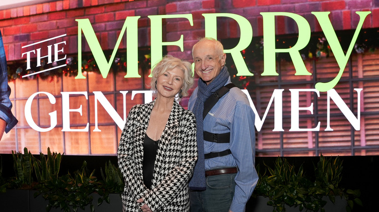Michael Gross stands smiling wearing a scarf next to his co-lead at the Netflix movie premiere of "The Merry Gentlemen"