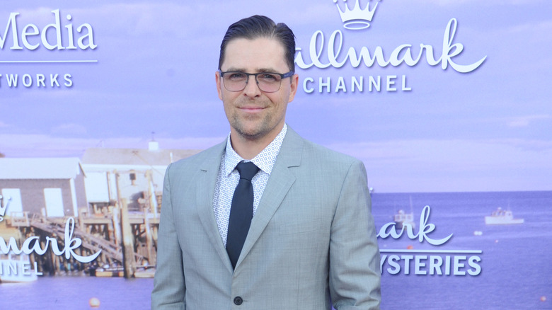 Kevan Smith smiling in a suit and glasses against a Hallmark backdrop.