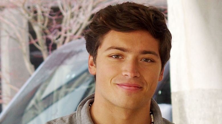 Joaquin Consuelos smiling on the set of the pilot "Foster Dade" while wearing a gray sweatshirt