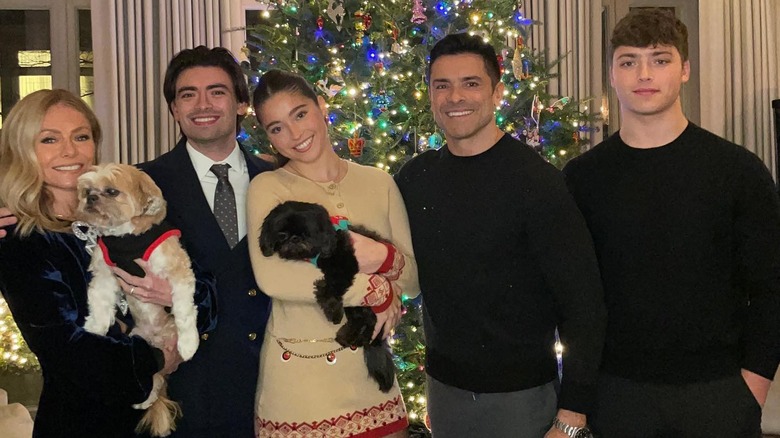 Kelly Ripa and Mark Consuelos smiling with their children in front of a Christmas tree holding their two dogs