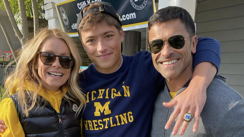Joaquin Consuelos smiling with his arms around his parents' shoulders showing off his Big Ten wrestling championship ring