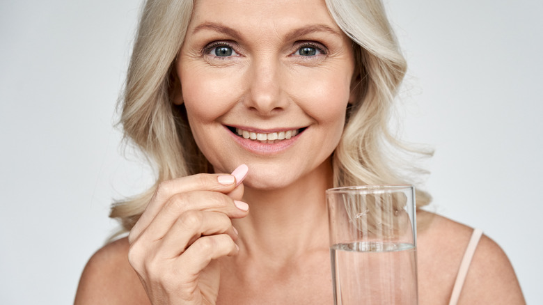 Smiling woman taking supplement with galss of water