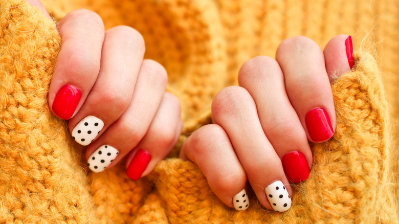 Woman with colorful manicured nails against a chunky knit yellow sweater.