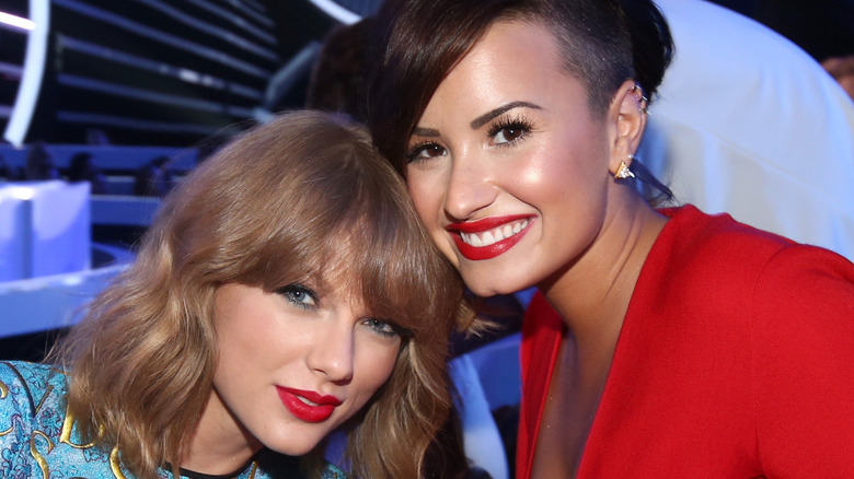 Taylor Swift smiles in blue with Demi Lovato in red.