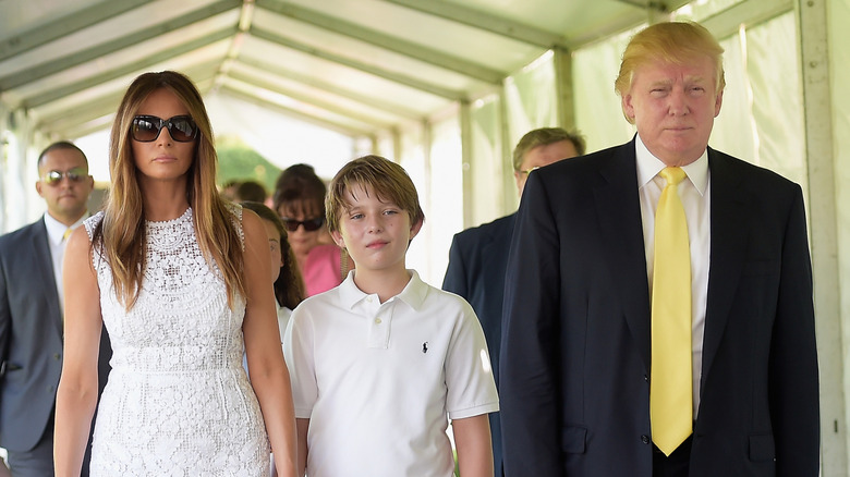 Melania and a young Barron Trump holding hands walking next to Donald Trump