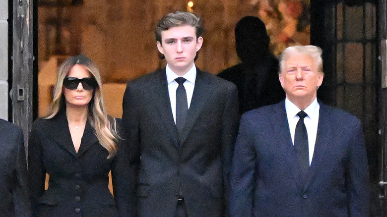 Melania, Barron, and Donald Trump standing in front of church at his grandmother's funeral