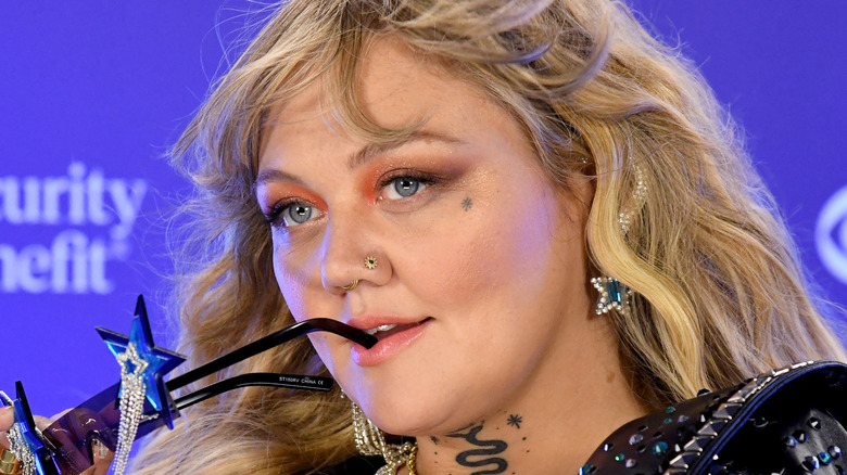 Elle King bites the arm of her sunglasses.