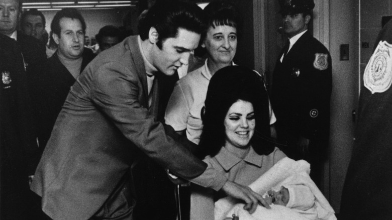 Elvis Presley touching baby in Priscilla's arms