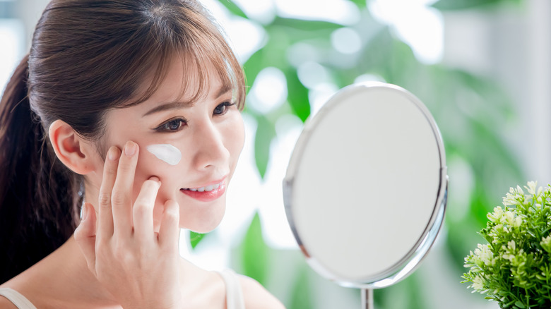 A woman looking at herself in the mirror while applying sunscreen on her face